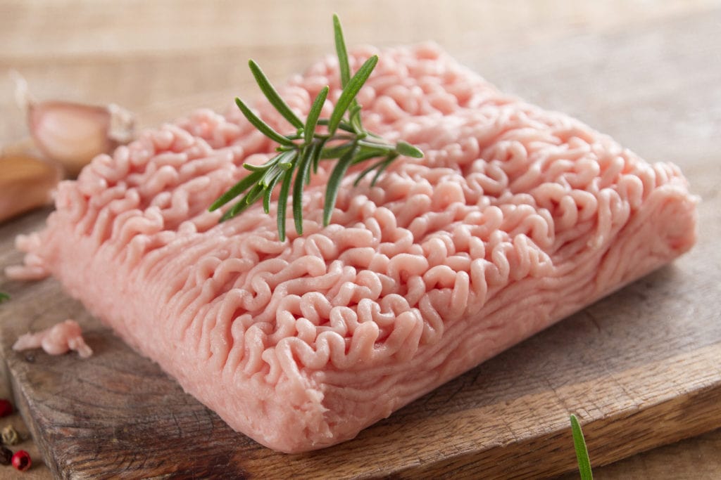 Minced chicken or turkey meat Minced chicken or turkey meat on wooden board with basil and spices, selective focus